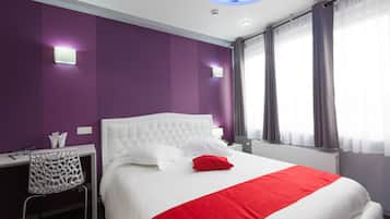 A hotel room with a white bed, purple walls, and a red accent on the bedspread.