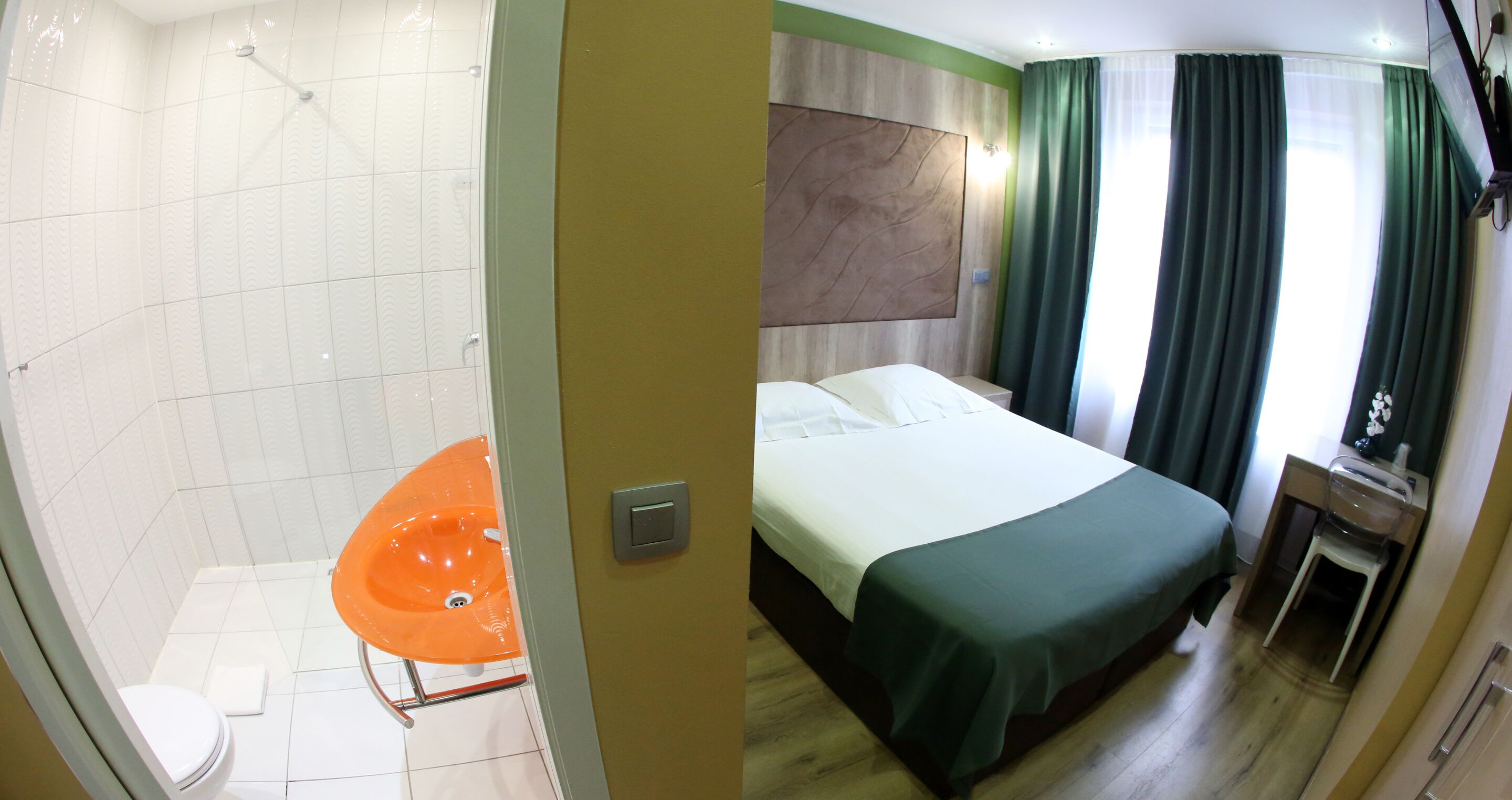 Habitación de hotel con ducha, inodoro, cama y un pequeño escritorio con espejo.