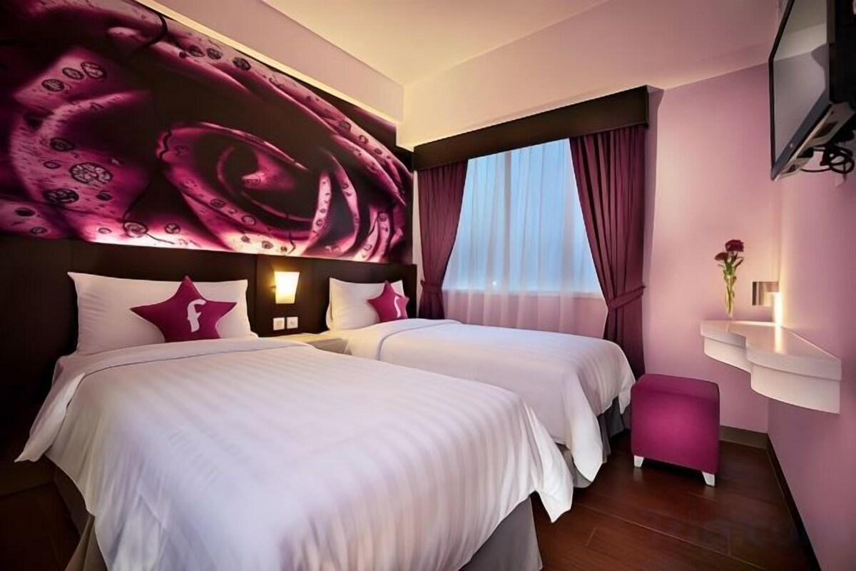 Habitació d'hotel amb dos llits, un mural gran a la paret, una televisió i una finestra amb cortines.