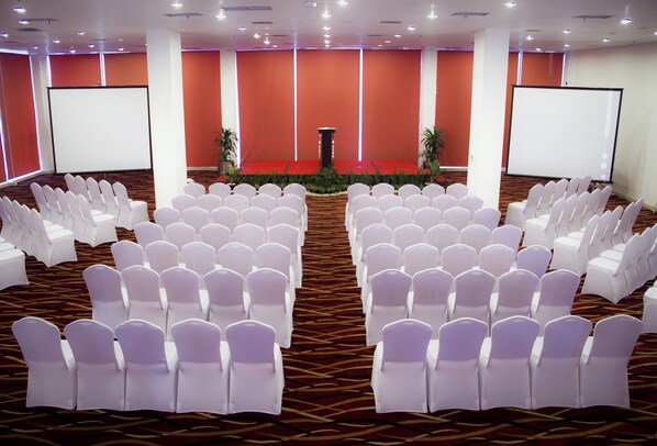 A conference room with rows of white chairs, a podium, and two projection screens.