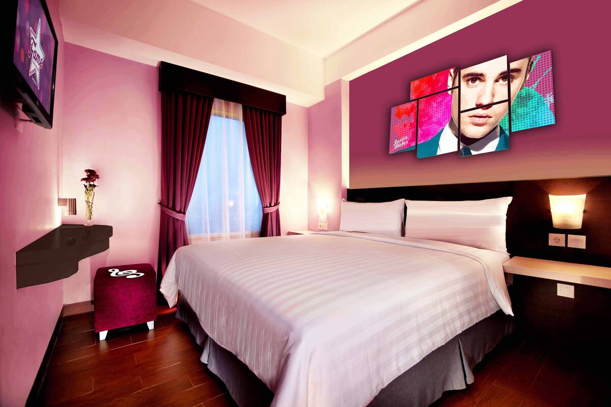 Quarto de hotel moderno com uma cama grande, uma toucador com espelho e uma TV fixada na parede.