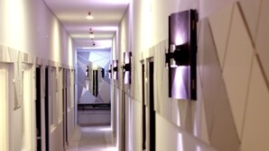 A long, narrow hallway with doors on both sides, leading to a central area with a geometric wall design. - Hotel Neo Kuta Jelantik (Legian)