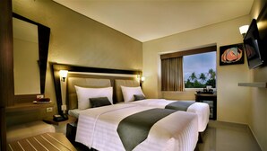A hotel room with two beds, a bedside table with a lamp, a small table with a telephone, and a window with a view of palm trees. - Hotel Neo Kuta Jelantik (Legian)