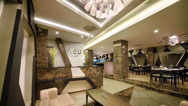 A modern hotel lobby with a reception desk, seating area, and a dining section. - Hotel Neo Kuta Jelantik (Legian)