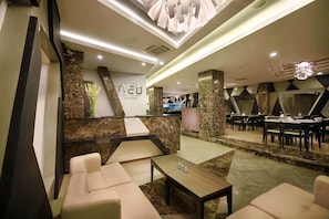 A modern hotel lobby with a reception desk, seating area, and a dining section. - Hotel Neo Kuta Jelantik (Legian)