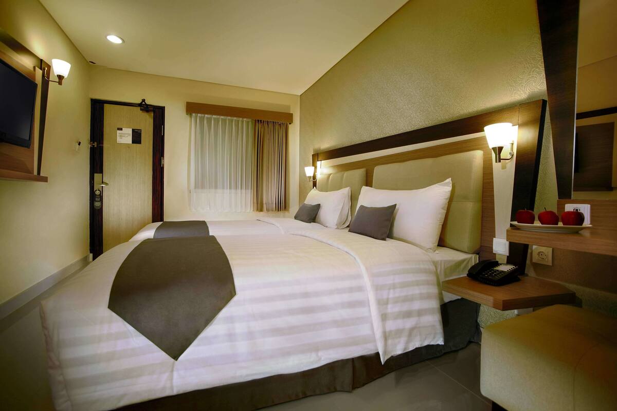 A hotel room with two beds, a television, a bedside table with a phone, and a window with curtains.
