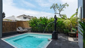 A swimming pool with a tiled edge, surrounded by a bamboo fence, a statue, and several potted plants. - Hotel Neo Kuta Jelantik (Legian)