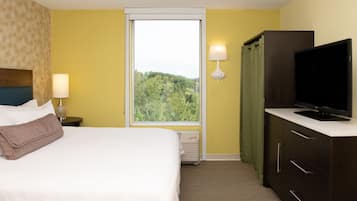A hotel room with a bed, a television, a nightstand, a lamp, and a window with a view of trees.