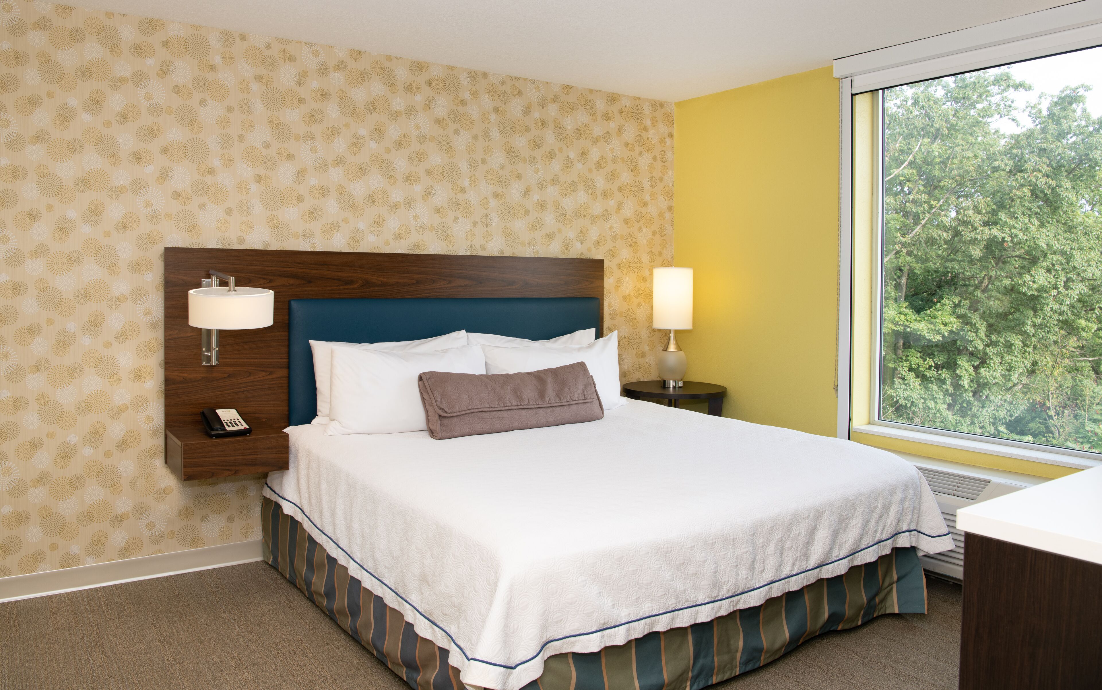 A hotel room with a bed, two bedside lamps, a phone, and a window with a view of trees.