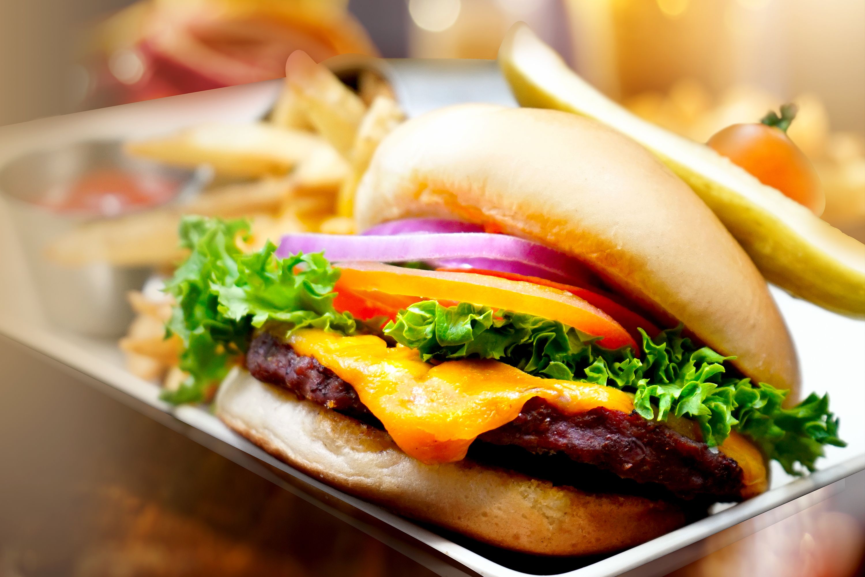 Una hamburguesa con lechuga, tomate y queso, acompañada de papas fritas y un pepinillo.