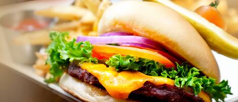 Una hamburguesa con lechuga, tomate y queso, acompañada de papas fritas y un pepinillo.