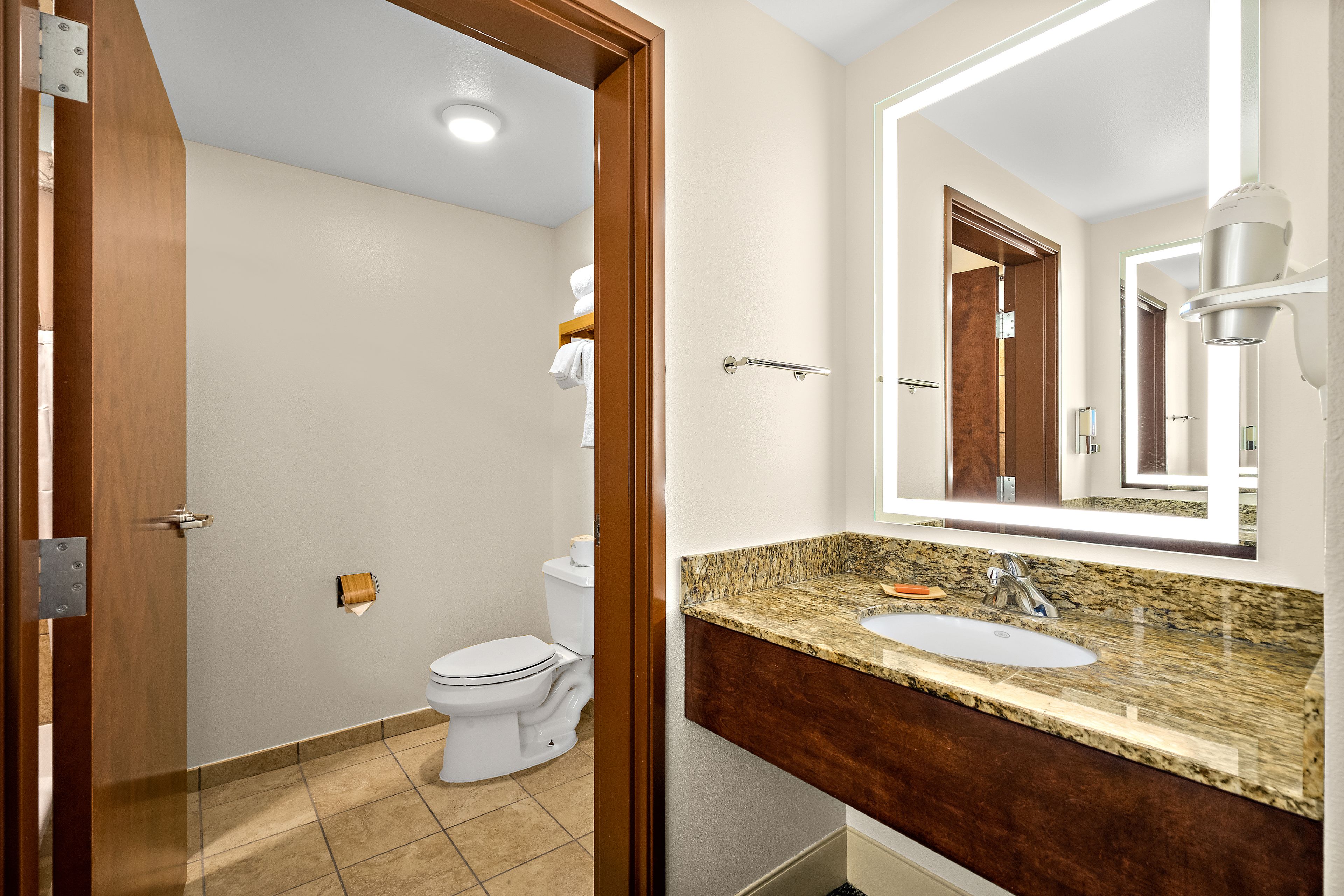 A modern bathroom with a white toilet, a sink with a granite countertop, and a mirror above the sink.