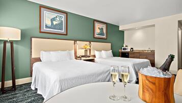 Ett hotellrum med två sängar, ett matbord med champagneglas och en minibar.