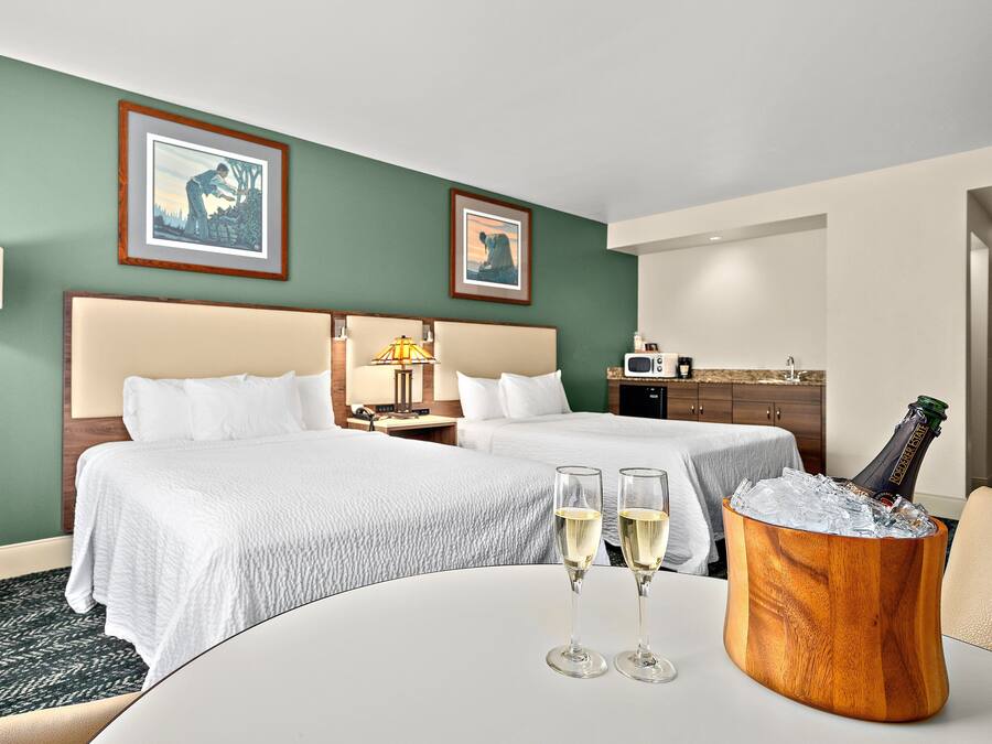 Ett hotellrum med två sängar, ett matbord med champagneglas och en minibar.