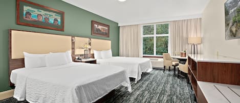 Habitación de hotel con dos camas, un escritorio, una silla y un amplio ventanal con cortinas.
