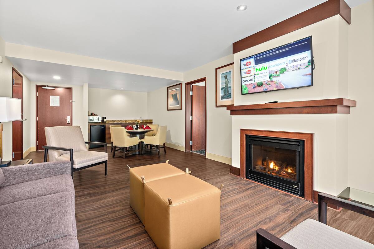 Habitación de hotel con televisión de pantalla plana, chimenea, comedor y zona de estar con sofá y reposapiés.