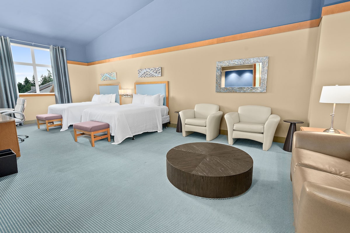 Una habitación de hotel con una cama, dos sillones, una mesa de centro redonda y un escritorio con una silla.