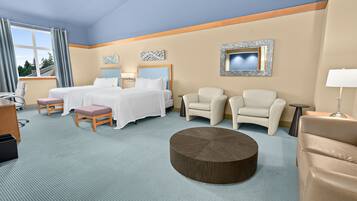 Quarto de hotel com uma cama, duas poltronas, uma mesa de centro redonda e uma escrivaninha com cadeira.