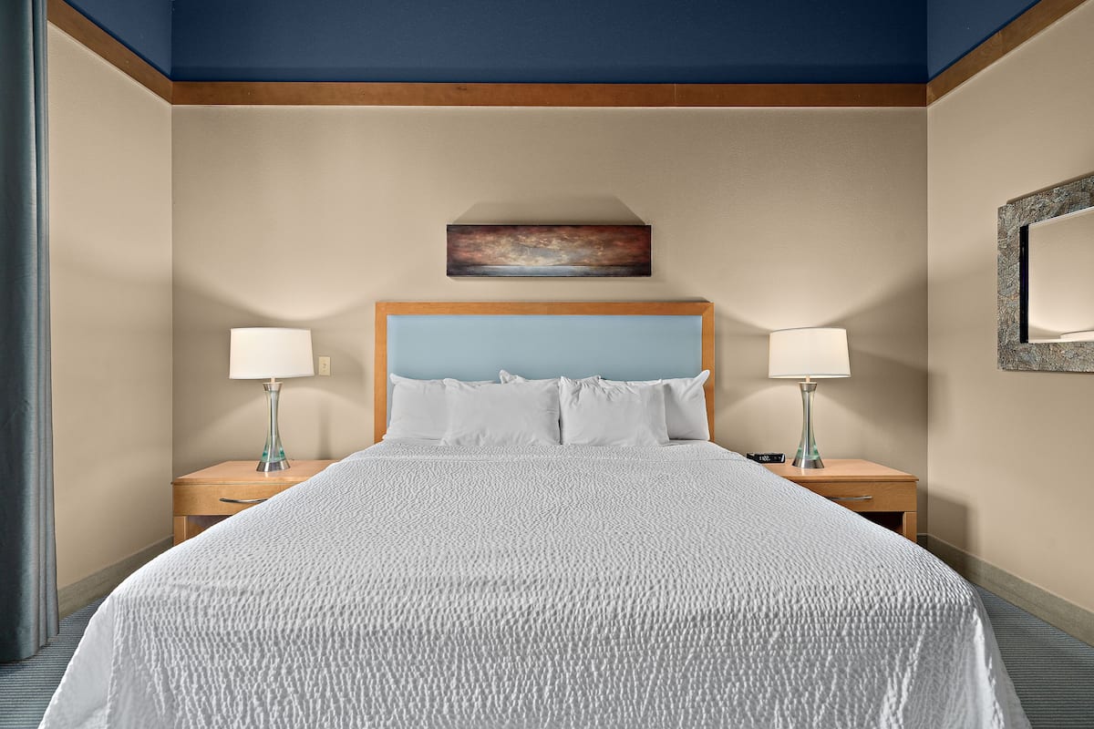 Una habitación de hotel con una cama grande, dos mesitas de noche con lámparas, un cuadro sobre la cama y un espejo en la pared.