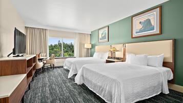A hotel room with two beds, a desk, a chair, a TV, and a window with a view of trees.