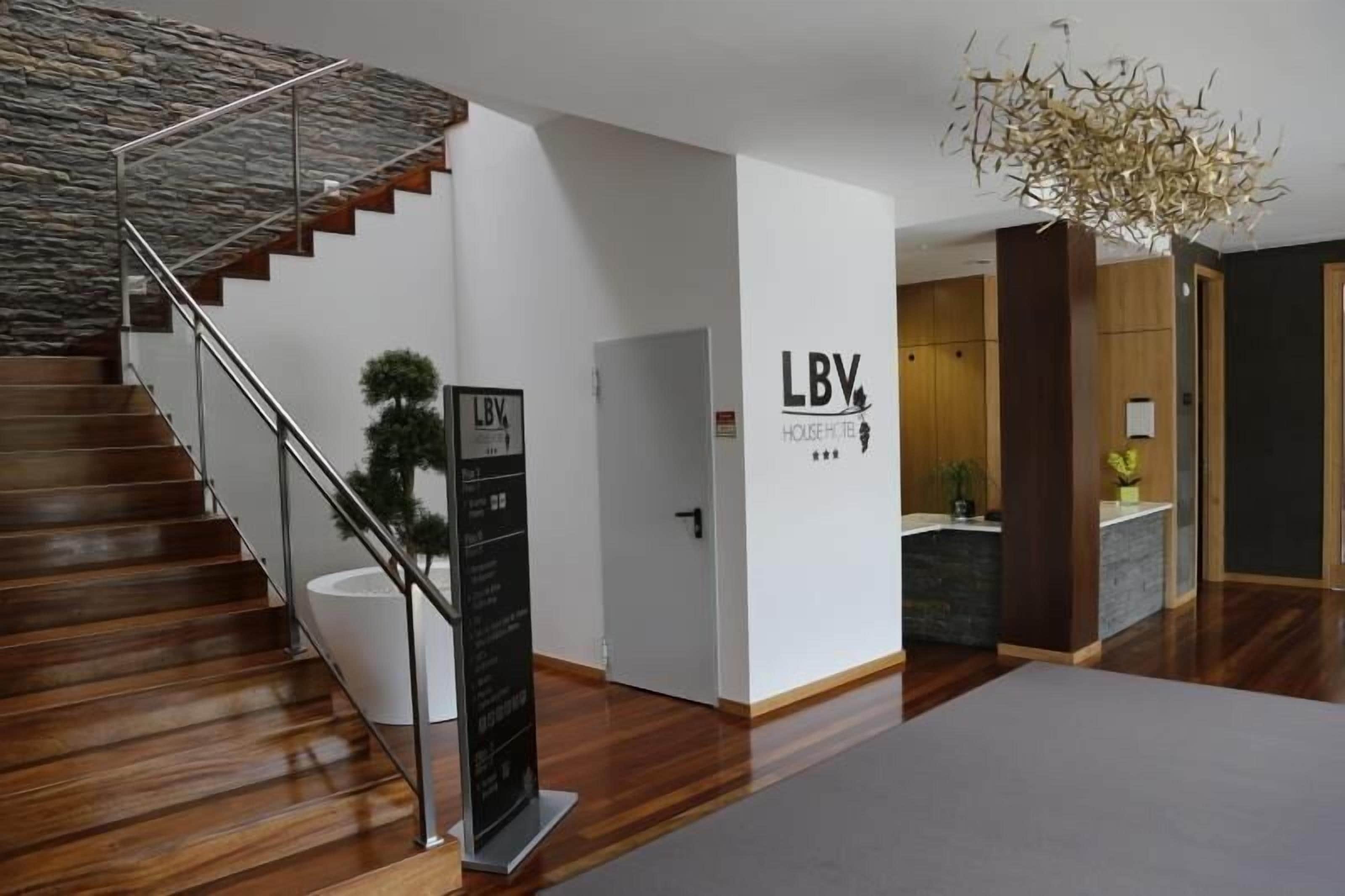 Un interior de hotel moderno con una escalera de madera, una pared de piedra y un letrero para LBV House Hotel.