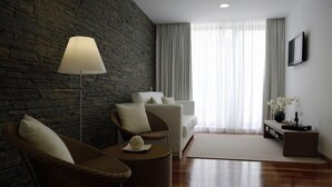 Una sala de estar moderna con una pared de piedra, un sofá, dos sillones, una mesa de centro, una lámpara de pie, un televisor y una ventana con cortinas.