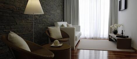 A modern living room with a stone wall, a sofa, two armchairs, a coffee table, a floor lamp, a TV, and a window with curtains.
