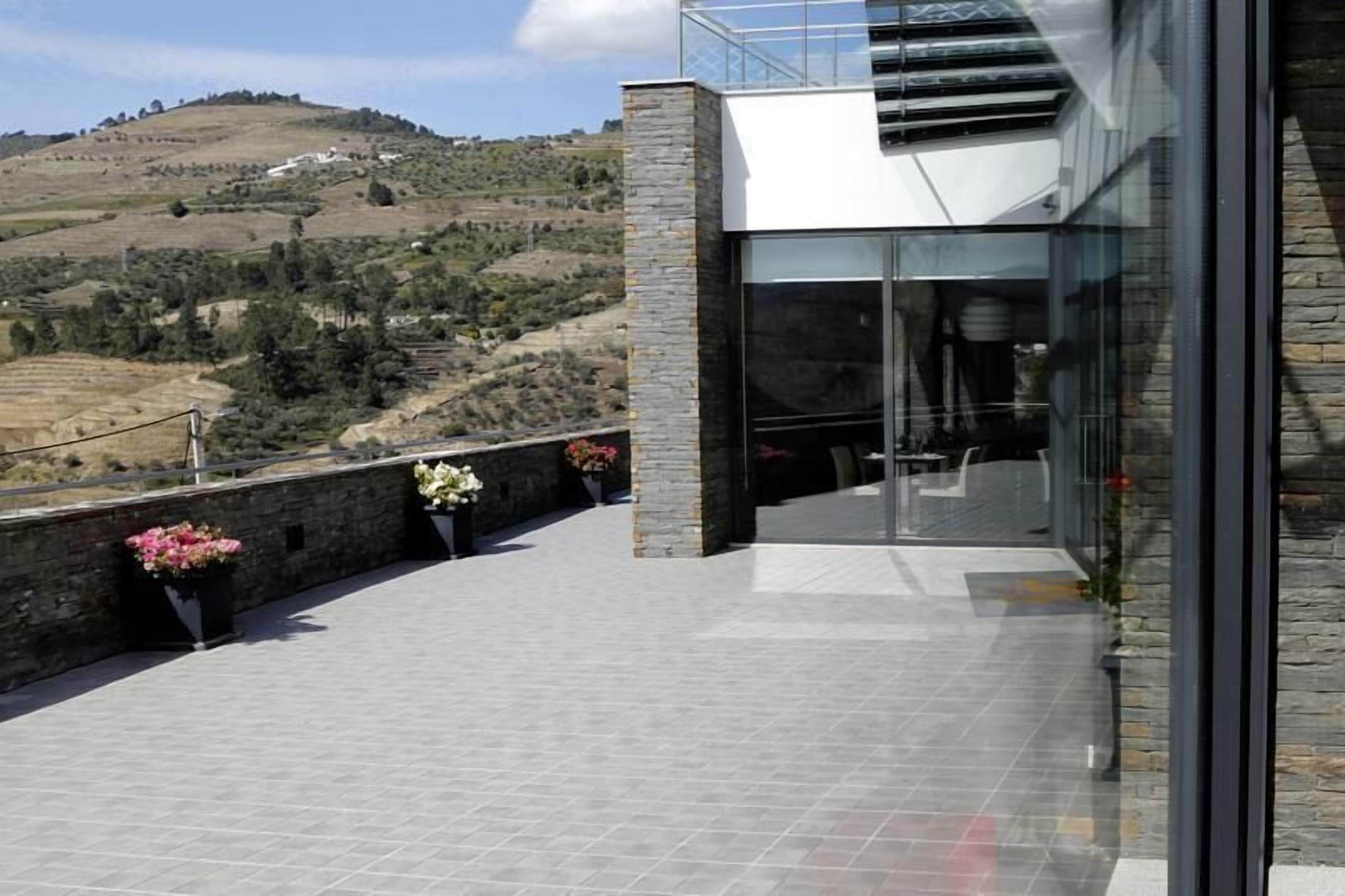 A modern building with a glass entrance, a stone wall, and potted plants.