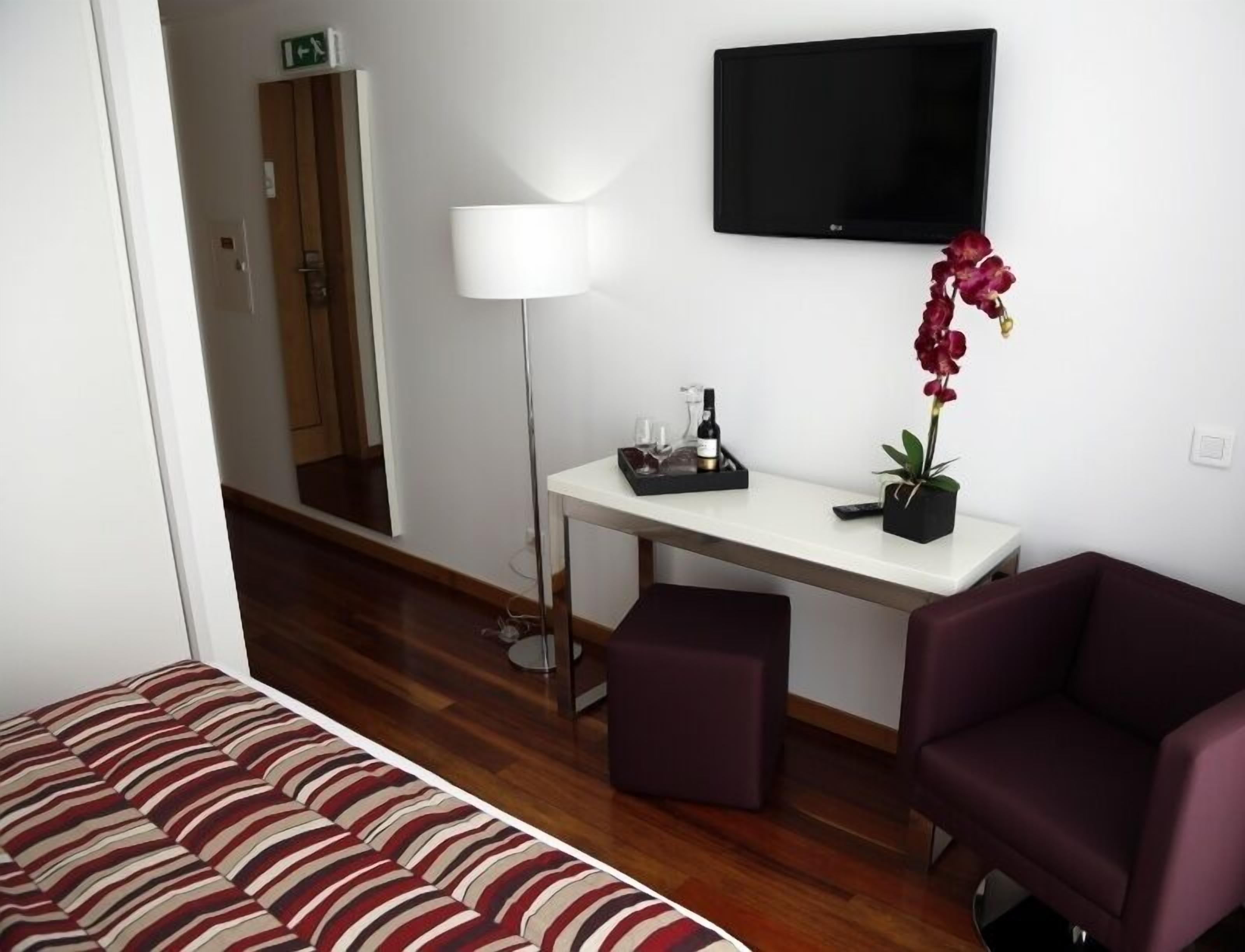 Habitación de hotel con cama, escritorio, silla, televisor y planta en maceta.