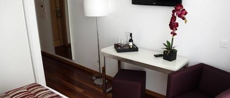 Habitación de hotel con cama, escritorio, silla, televisor y planta en maceta.