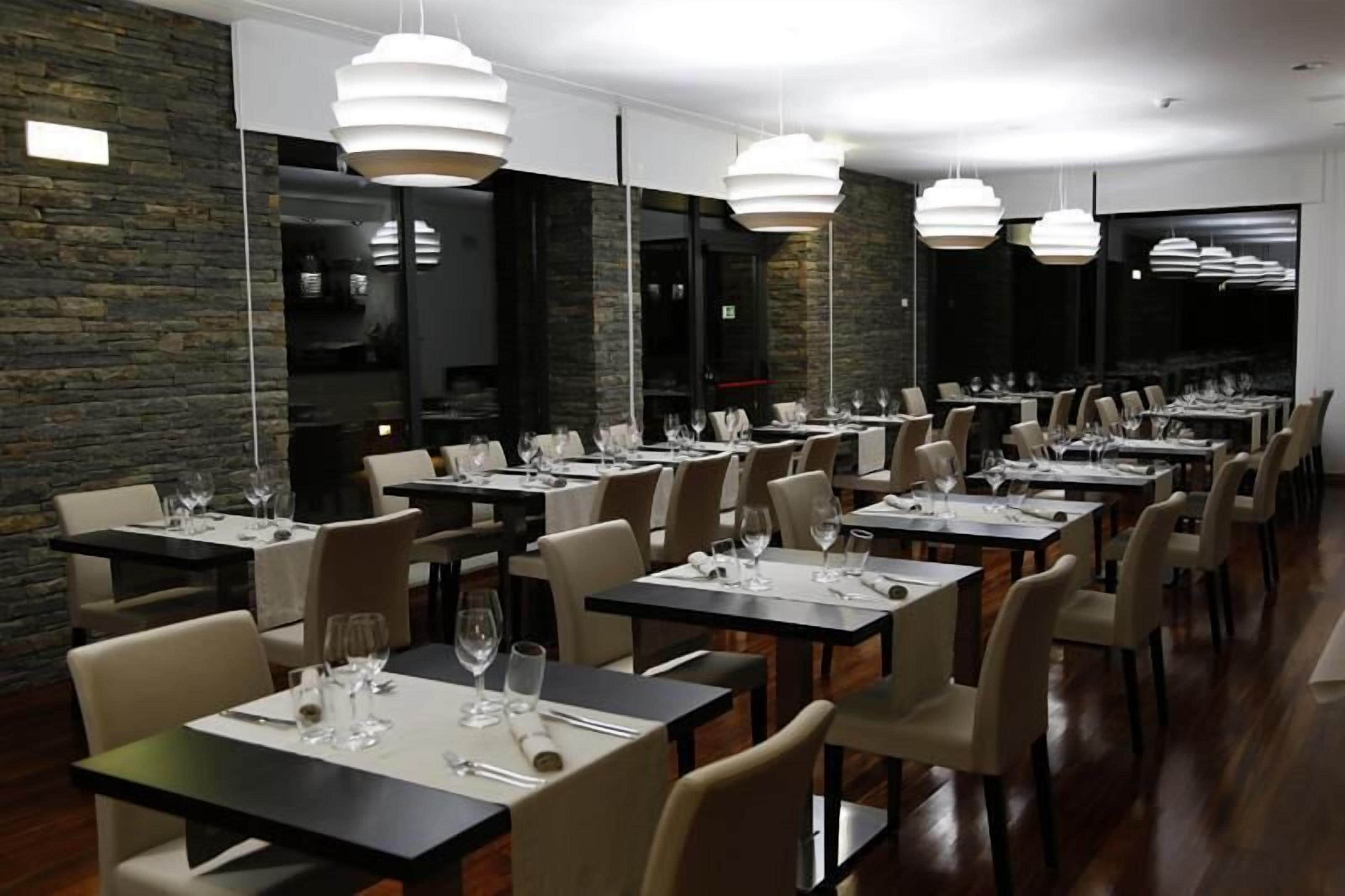 Un restaurante con varias mesas y sillas, iluminación colgante moderna y una pared de piedra.