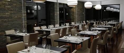 Un restaurante con varias mesas y sillas, iluminación colgante moderna y una pared de piedra.