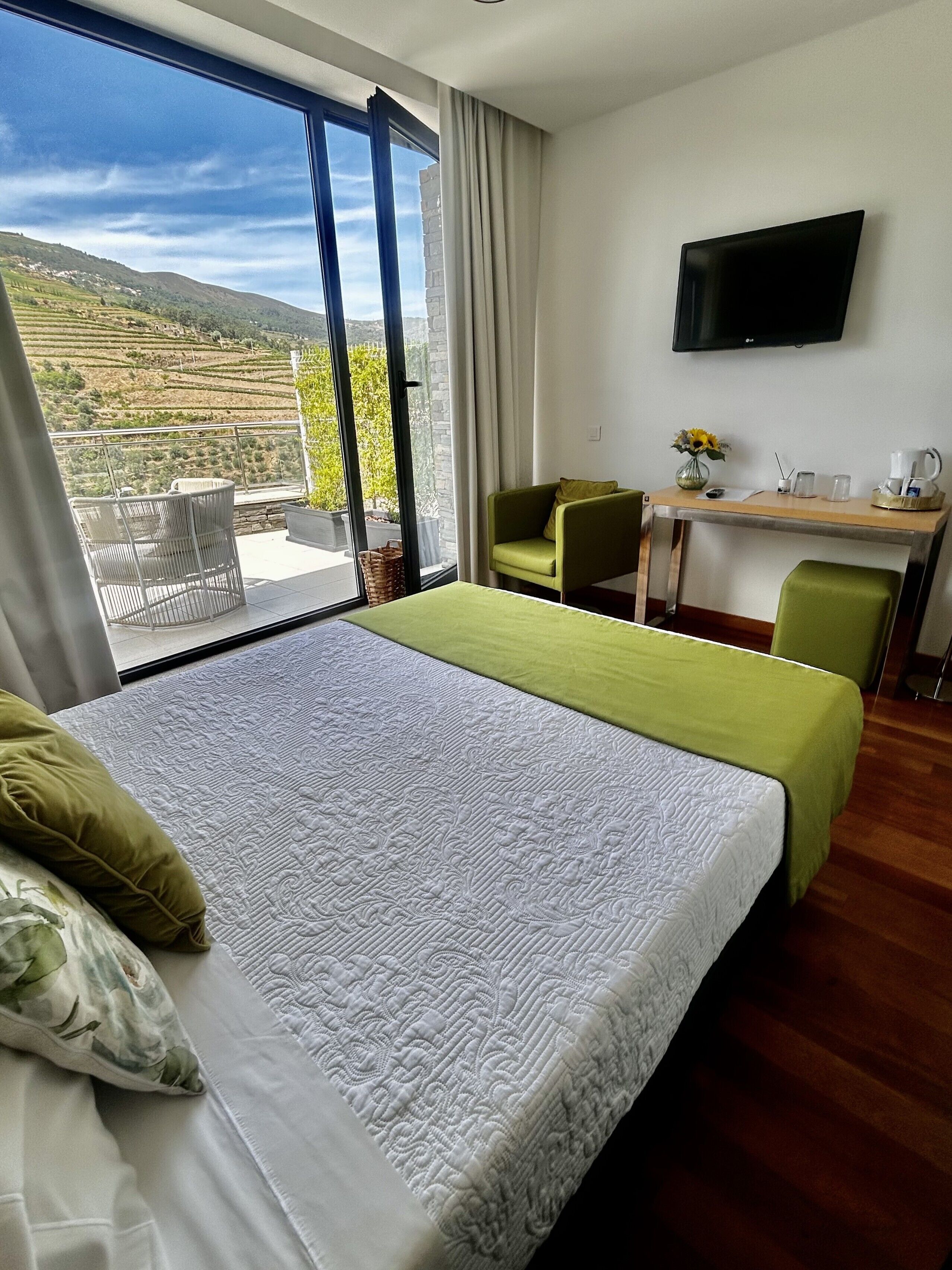 Een hotelkamer met een groot bed, een bureau, een stoel, een televisie en uitzicht op het landschap.