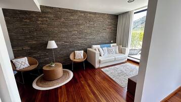 Ein modernes Wohnzimmer mit einer Steinwand, einem weißen Sofa, einem runden Wickertisch und einer Stehlampe.