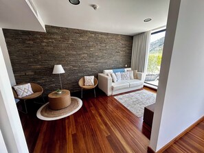 A modern living room with a stone wall, a white sofa, a round wicker side table, and a floor lamp. - LBV House Hotel (Alijó)