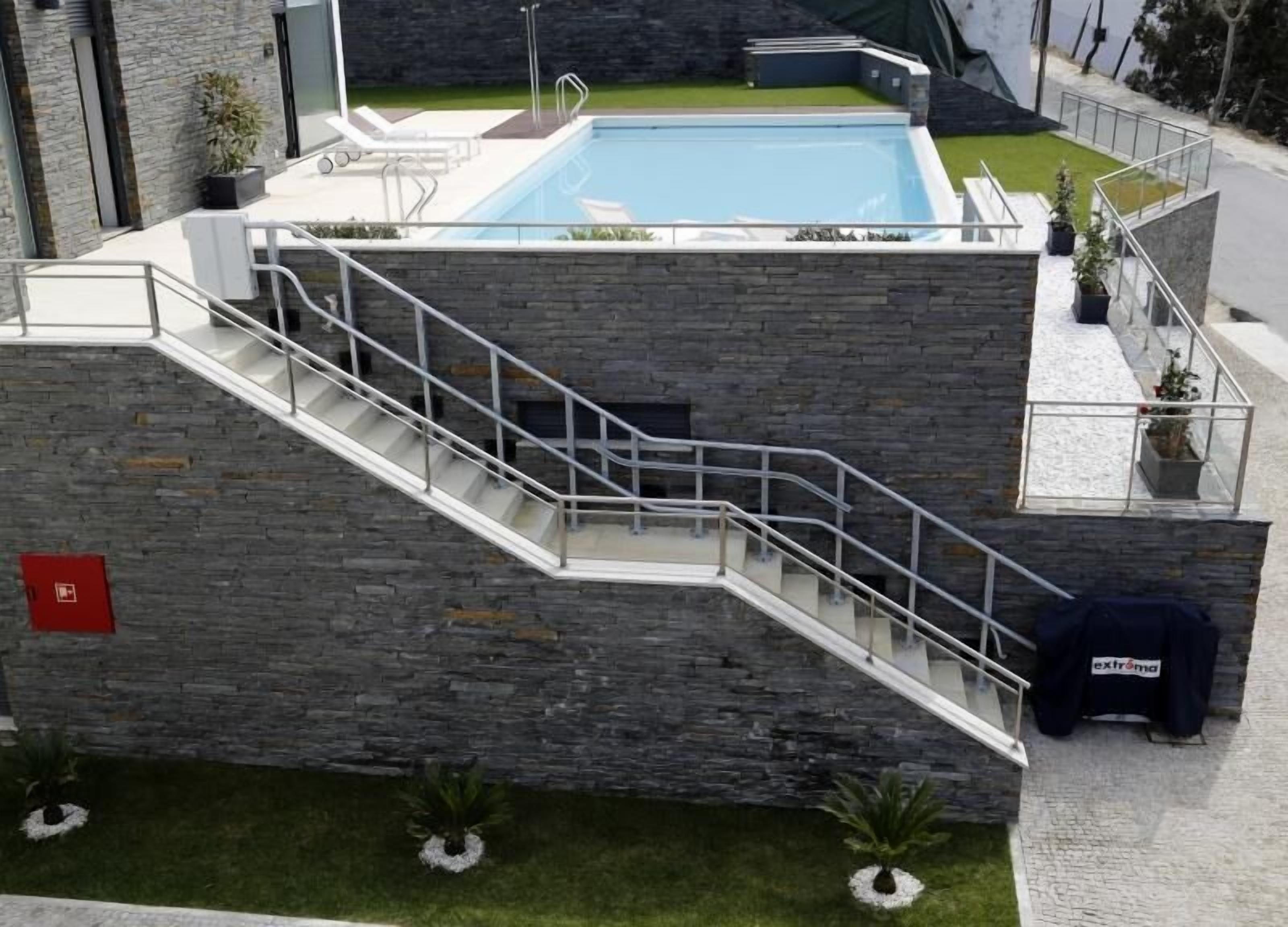 A modern building with a stone facade, a pool, and a staircase leading to a rooftop area.