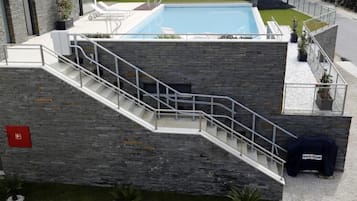 A modern building with a stone facade, a pool, and a staircase leading to a rooftop area.