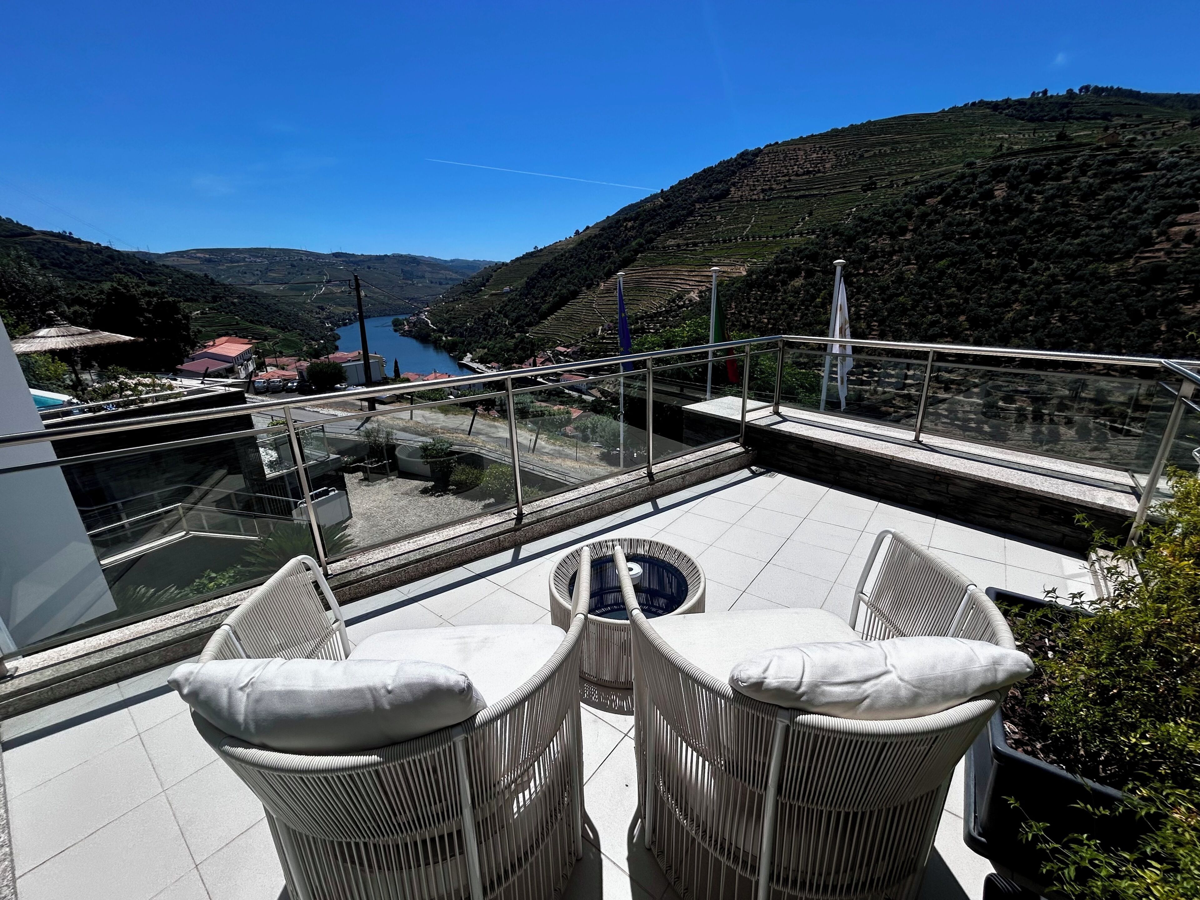 Une terrasse avec des chaises en osier et une vue sur une vallée et une rivière.