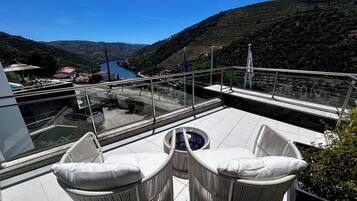 Une terrasse avec des chaises en osier et une vue sur une vallée et une rivière.