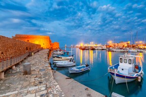 A harbor with boats docked, a stone wall, and a castle-like structure in the background.