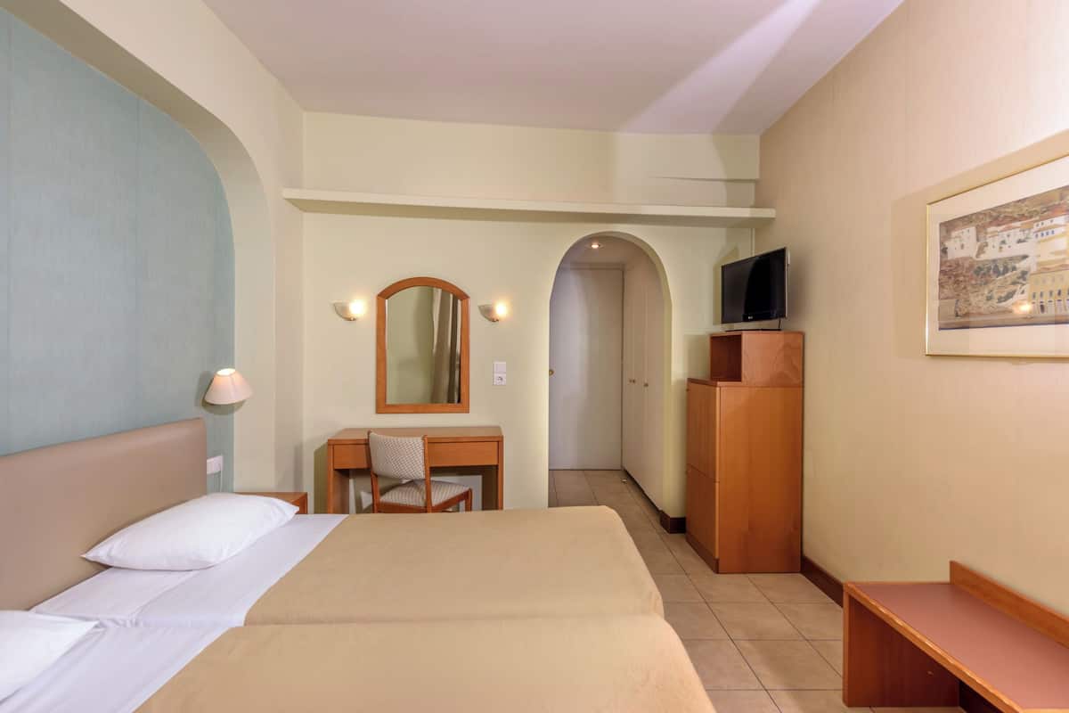 A hotel room with a bed, a desk with a chair, a TV on a wooden cabinet, and a framed picture on the wall.