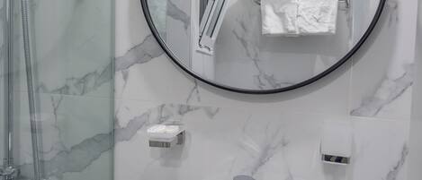 A bathroom with a white sink, a round mirror, and a glass-enclosed shower.