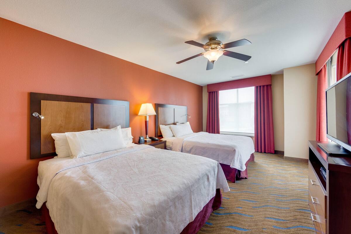 Une chambre d’hôtel avec deux lits, un ventilateur de plafond, une télévision et une fenêtre avec des rideaux.