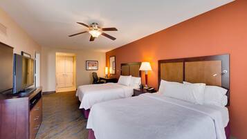 A hotel room with two beds, a ceiling fan, a TV, a desk, and a lamp.