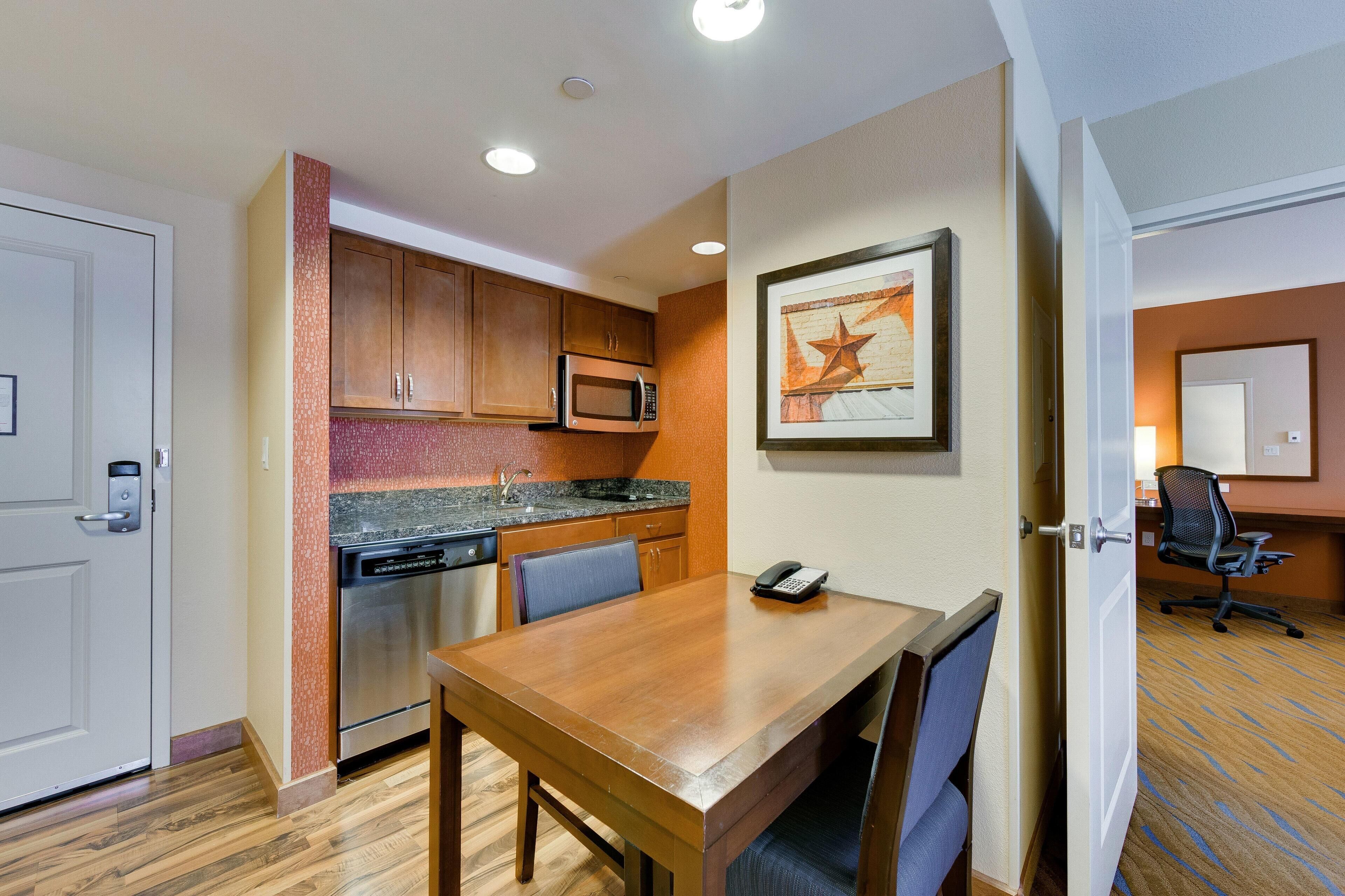 Une chambre d’hôtel équipée d’une table à manger en bois, d’un four à micro-ondes, d’un évier et d’une chaise.
