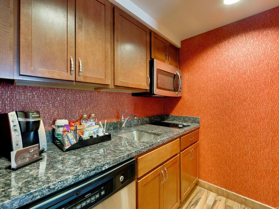 A kitchen with wooden cabinets, a built-in microwave, a coffee maker, and a dishwashing unit.