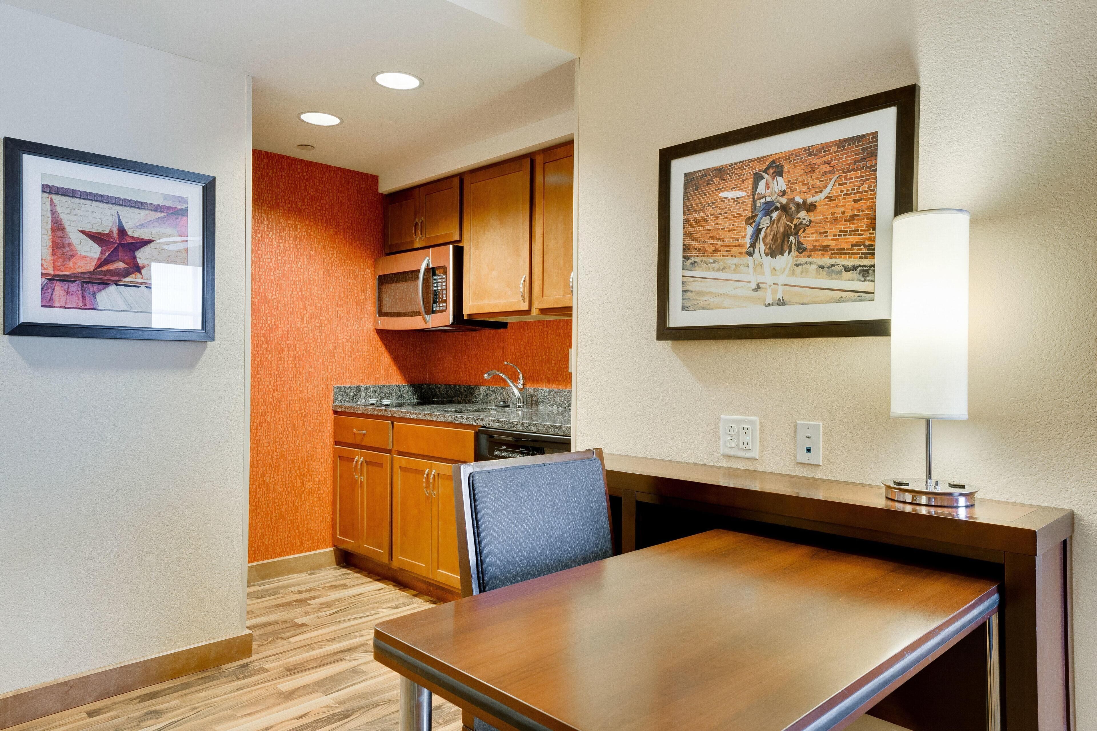 Una habitación de hotel con una mesa de comedor de madera, un microondas y un lavabo en la cocina.