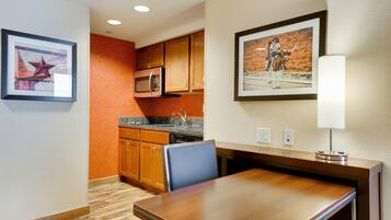 Una habitación de hotel con una mesa de comedor de madera, un microondas y un lavabo en la cocina.