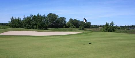 Un campo de golf con un búnker de arena, un mástil de bandera y cielo despejado.