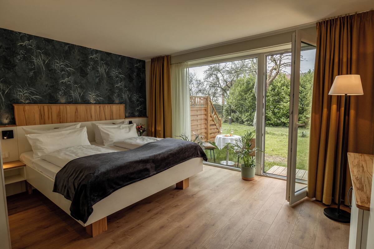 A bedroom with a large bed, wooden headboard, and a view of a garden through a sliding glass door.